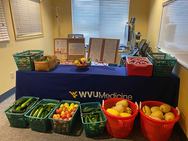 A Farm to You pickup table.  The table has a WVU blue table cloth with the WVUMedicine branding present and a series of baskets filled with vegetables are present.